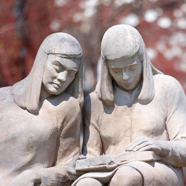 a close up of a statue depicting two girls, one reading and another looking over her shoulder at her book. 