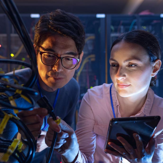 An east Asian man and a white woman inspect a server in computer server room.