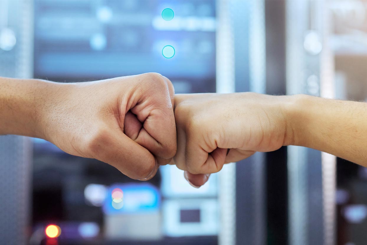 a fist bump occuring in front of a wall of computer hardware